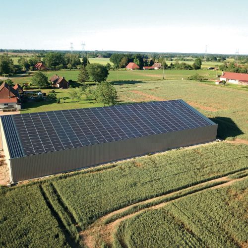 Bâtiment agricole avec toiture photovoltaïque par Le Triangle, intégré harmonieusement dans un paysage rural vaste et ouvert.