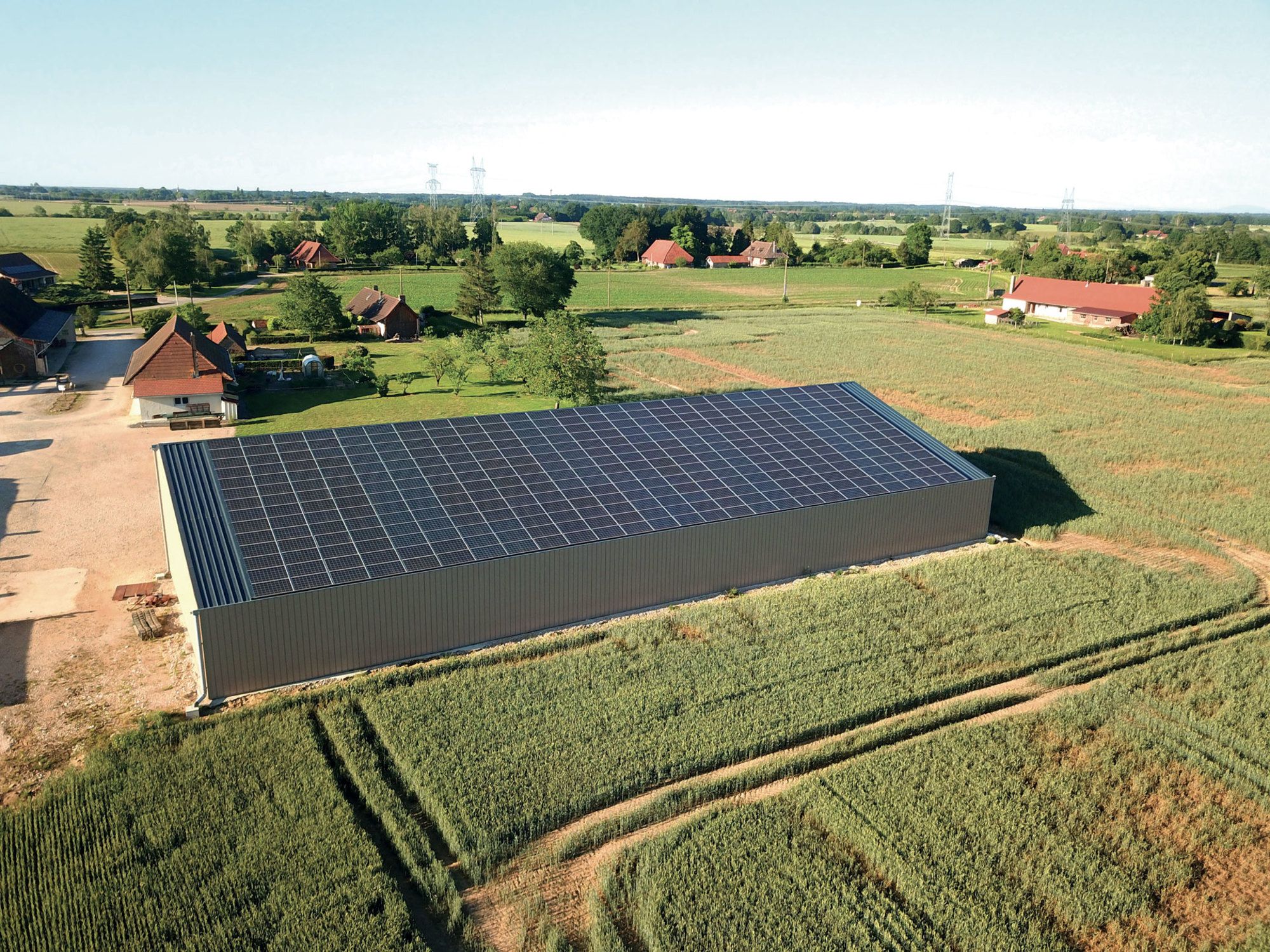 Bâtiment agricole avec toiture photovoltaïque par Le Triangle, intégré harmonieusement dans un paysage rural vaste et ouvert.